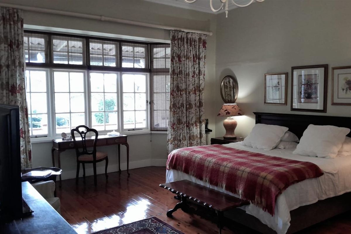 A spacious bedroom featuring polished timber flooring, large bay windows with natural light, and classic architectural detailing.