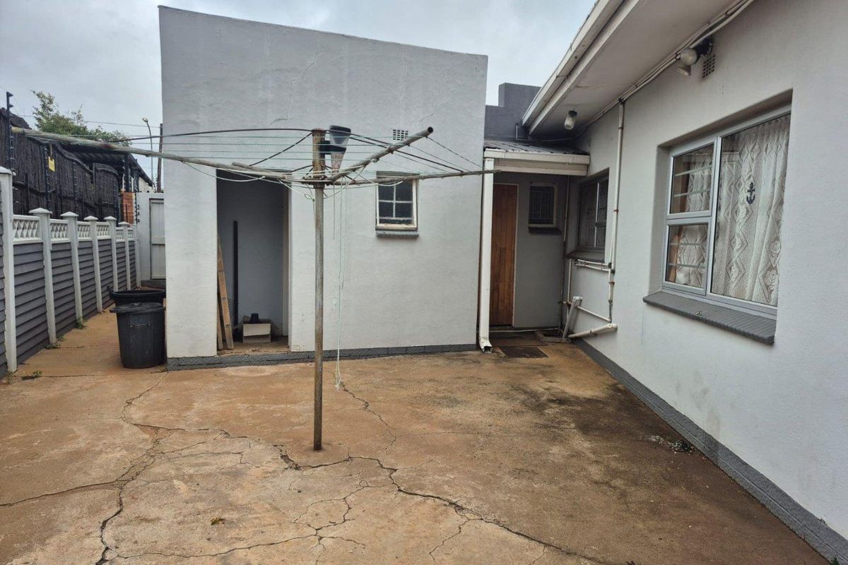 Rear exterior area featuring a concrete courtyard, utility access, and a rotary clothesline, showing signs of wear and weathering.