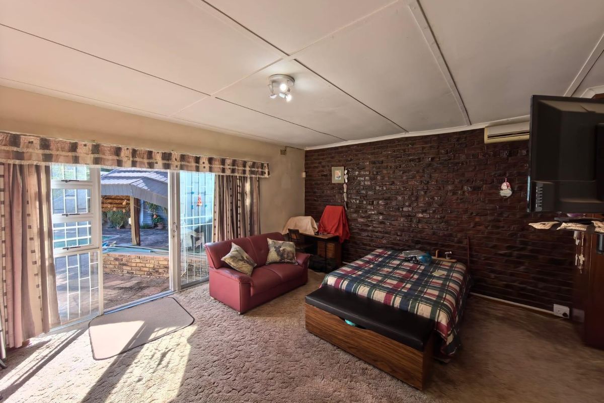Spacious bedroom featuring a rustic exposed brick feature wall, carpeted flooring, and sliding glass doors providing direct access to the outdoor patio area.