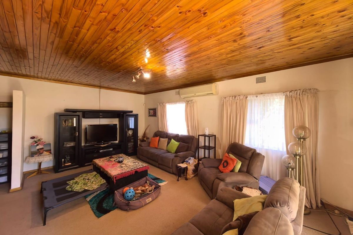 A spacious living room featuring a distinctive timber-paneled ceiling, wall-mounted air conditioning unit, and large windows allowing for natural light.