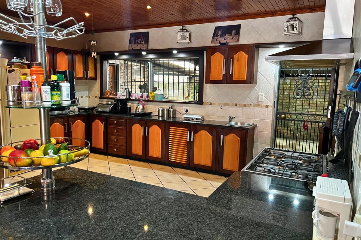 A functional kitchen featuring dark granite countertops, two-tone wooden cabinetry, a gas hob with extractor fan, and a timber-paneled ceiling.