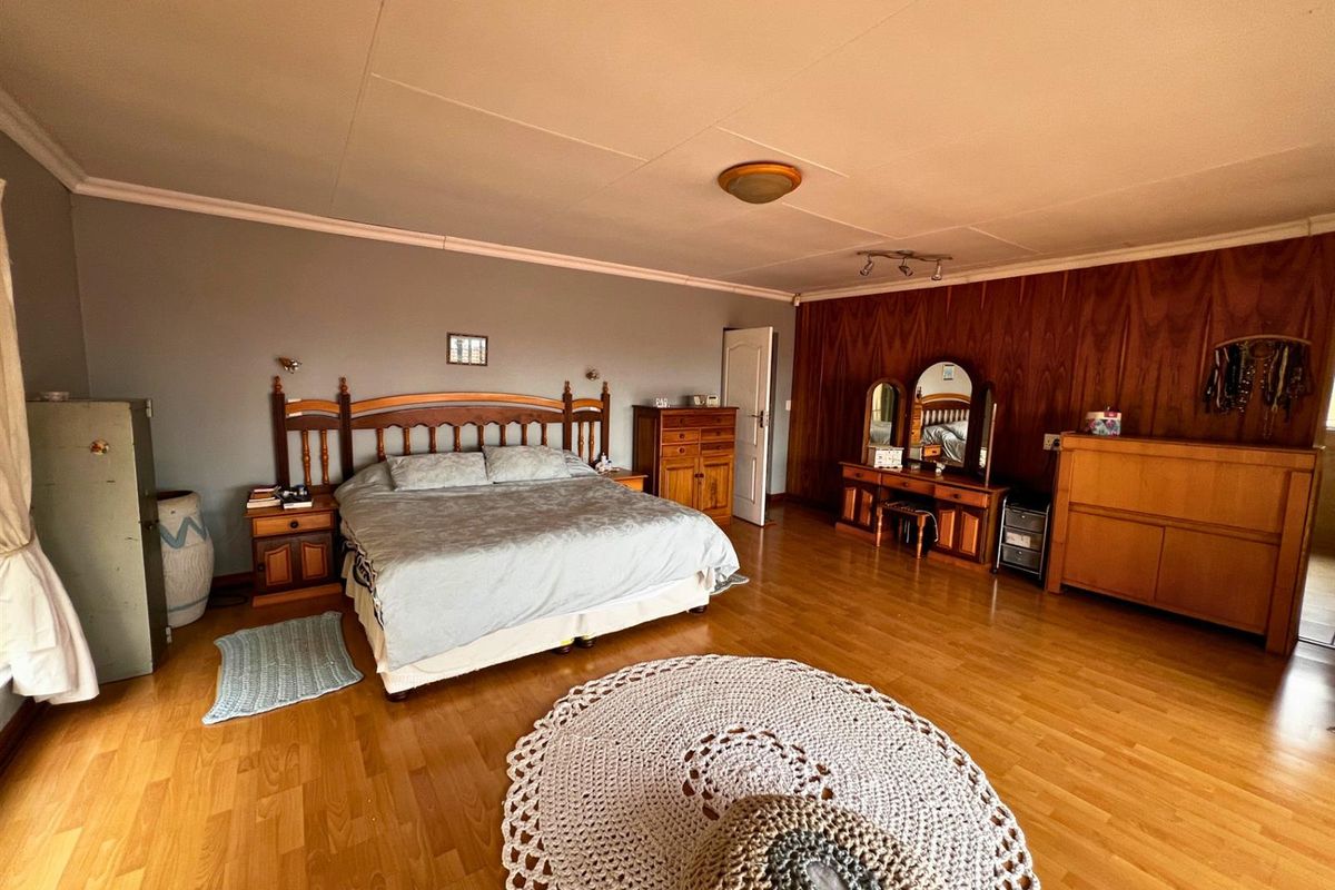 Spacious bedroom featuring wood-look laminate flooring and a combination of painted and wood-paneled walls.
