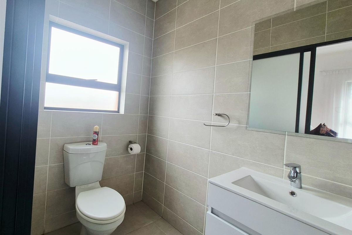 A modern bathroom featuring neutral wall tiles, a sleek vanity with integrated basin, a wall-mounted mirror, and a standard toilet.
