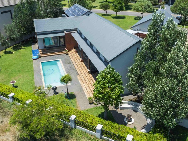 Aerial view of a modern residential property featuring a swimming pool, timber decking, solar panels, and a landscaped garden with a paved fire pit area.