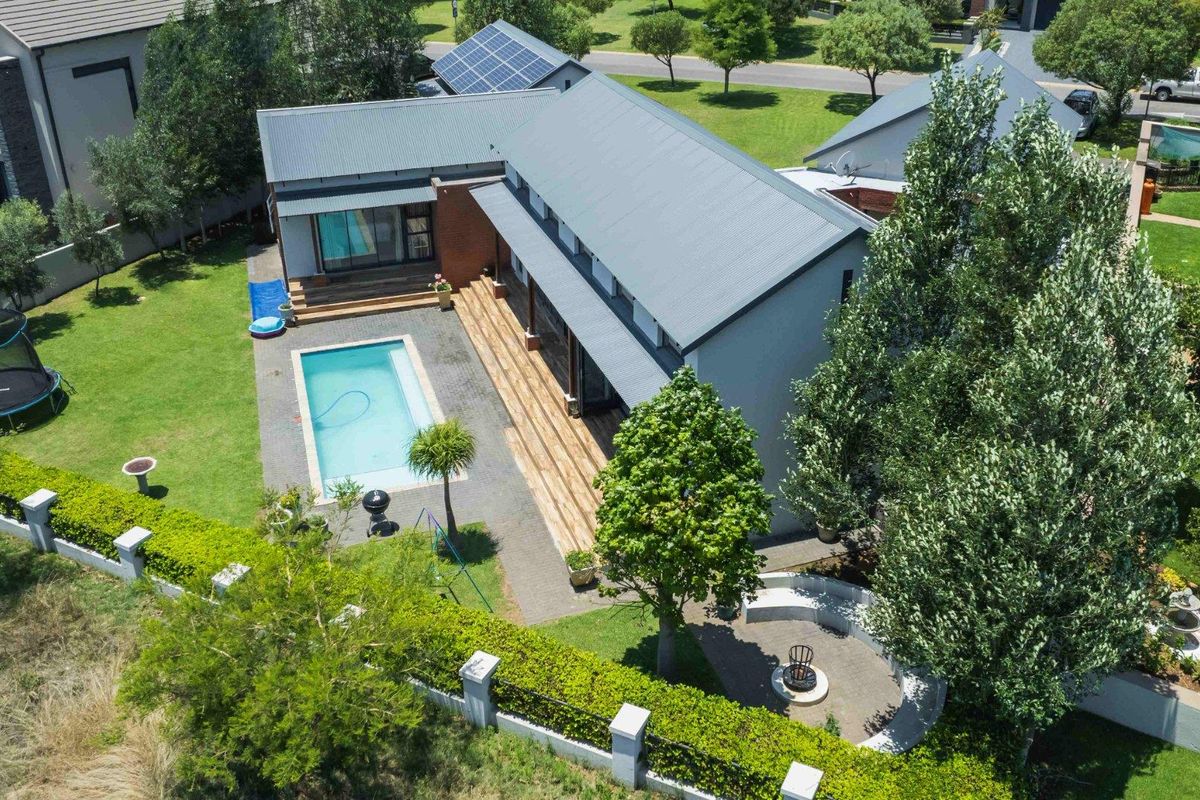 Aerial view of a modern residential property featuring a swimming pool, timber decking, solar panels, and a landscaped garden with a paved fire pit area.