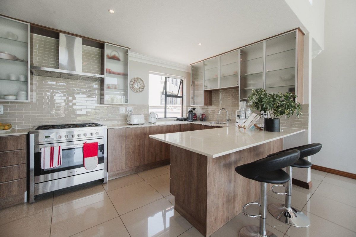 Modern kitchen featuring wood-finish cabinetry, quartz countertops, a stainless steel gas stove, and a subway tile backsplash with integrated lighting.