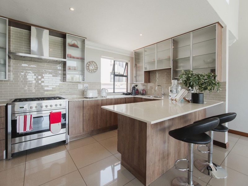 Modern kitchen featuring wood-finish cabinetry, quartz countertops, a stainless steel gas stove, and a subway tile backsplash with integrated lighting.