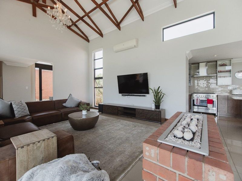 Spacious open-plan living area featuring high vaulted ceilings with exposed timber trusses, a built-in gas fireplace, and an integrated kitchen with modern finishes.