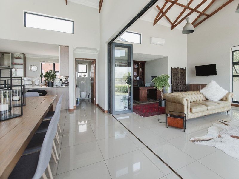 Spacious open-plan living area featuring vaulted ceilings with exposed timber trusses, sleek porcelain tiling, and seamless indoor-outdoor flow through large bi-fold glass doors.