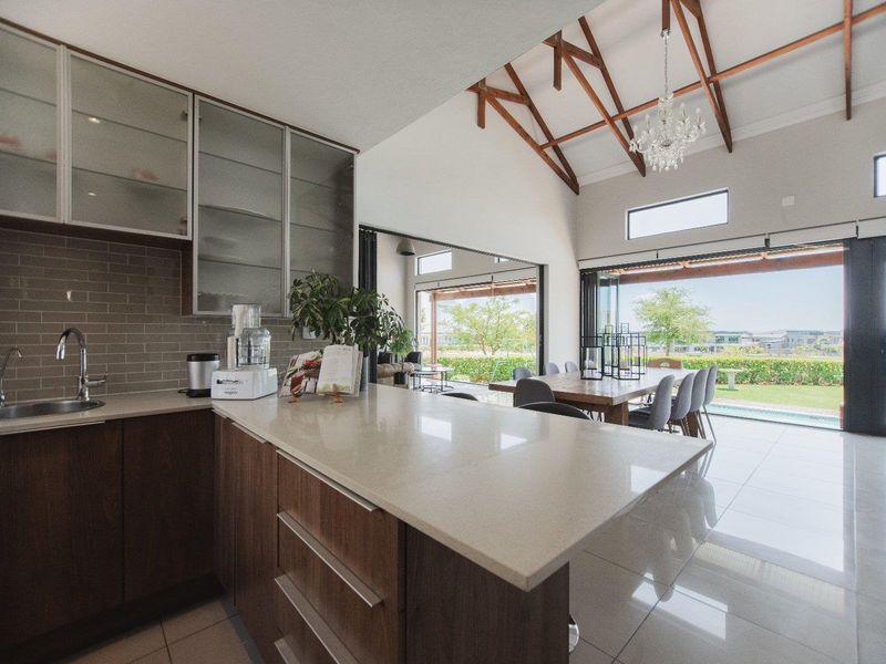 Modern open-plan kitchen and dining area featuring stone countertops, exposed timber trusses, and large stacking doors opening to the outdoor patio and pool.