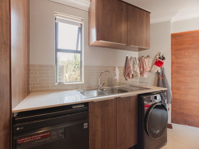 A functional laundry room featuring modern wood-finish cabinetry, a double sink with a stone countertop, and a subway tile backsplash.