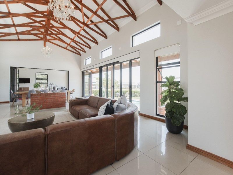 Spacious open-plan living area featuring high vaulted ceilings with exposed timber trusses, large stacking glass doors, and modern tiled flooring.