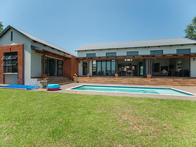 Rear view of the property featuring a swimming pool, expansive timber decking, covered patio area, and modern architectural design with exposed brick accents.
