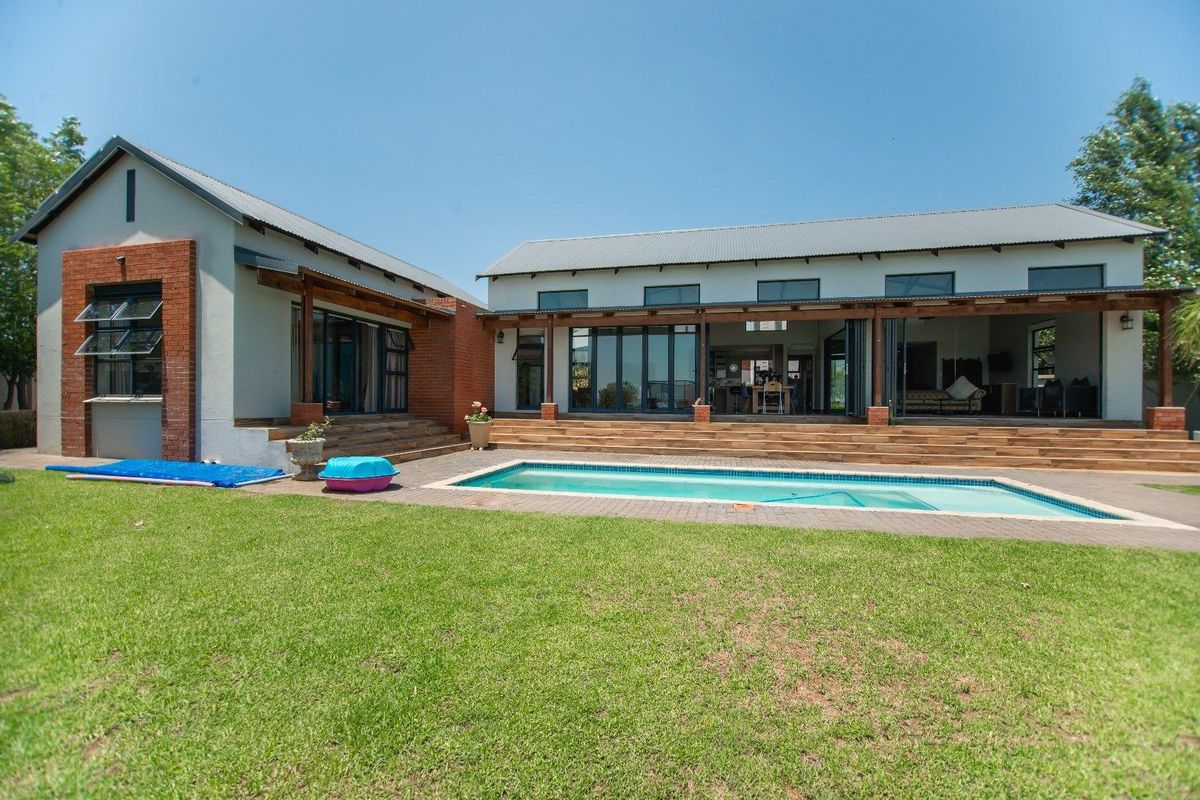 Rear view of the property featuring a swimming pool, expansive timber decking, covered patio area, and modern architectural design with exposed brick accents.