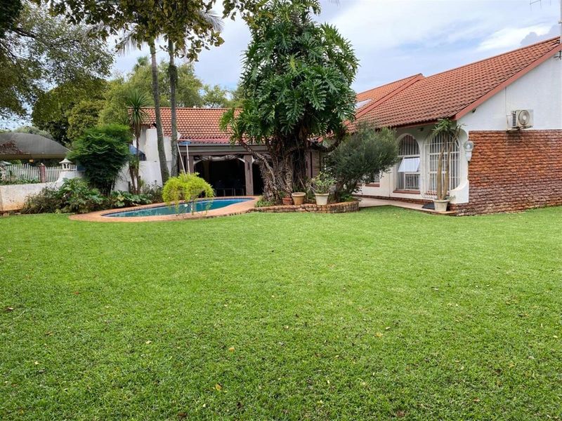 Spacious rear garden featuring a swimming pool, established trees, and a brick-accented house exterior with a tiled roof.