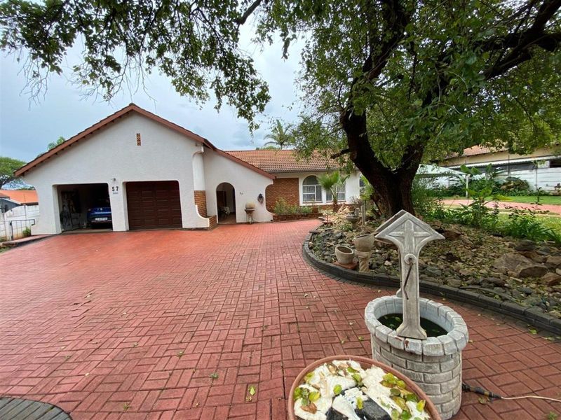 Front exterior view of a single-story house featuring a paved driveway, integrated garage, and established garden with a decorative stone well feature.
