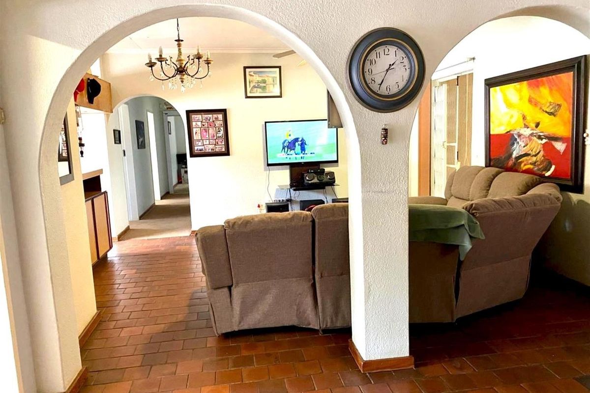 A living room area featuring traditional arched doorways, terracotta tile flooring, and a central hallway leading to other parts of the home.