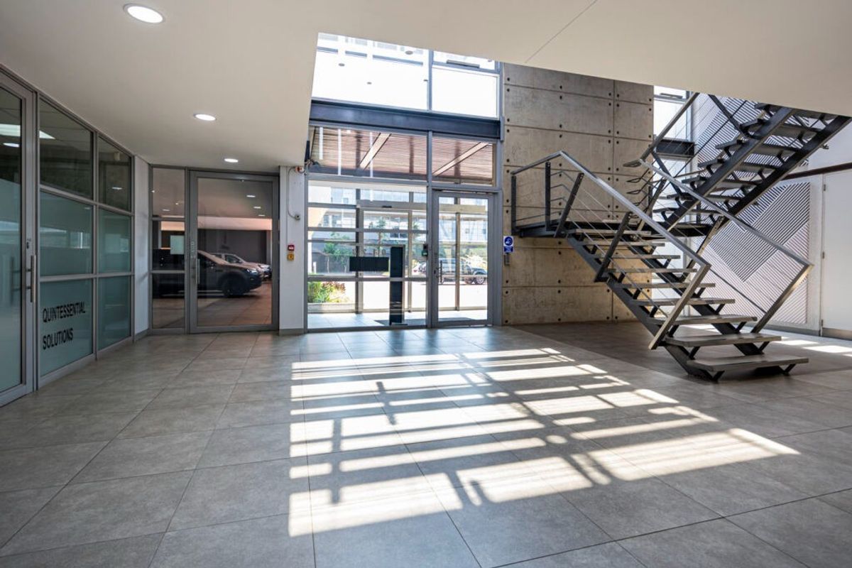 Modern commercial entrance lobby featuring large glass doors, tiled flooring, and a striking industrial-style steel staircase against a concrete feature wall.