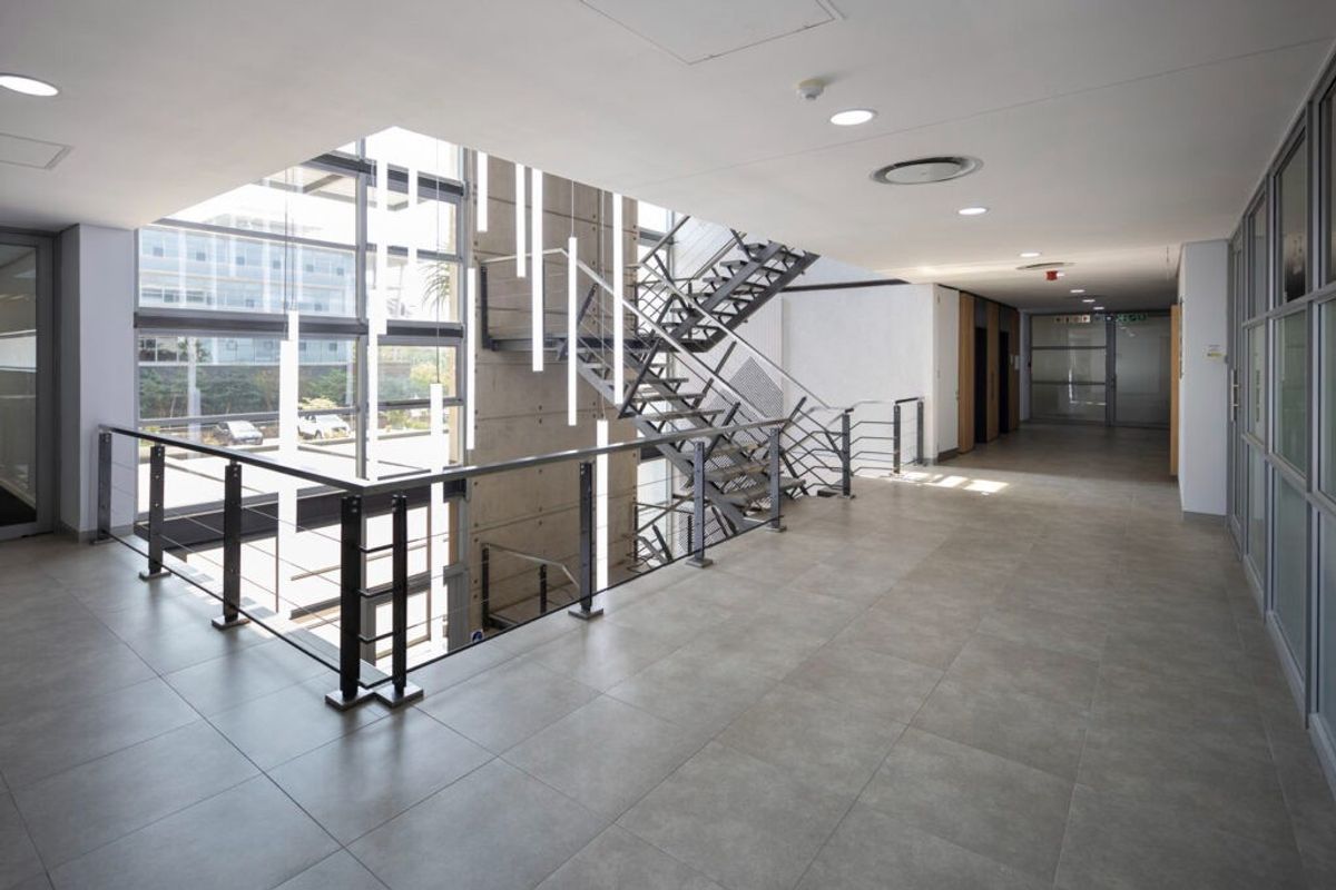 Modern commercial hallway featuring large glass windows, exposed concrete wall, and a contemporary metal staircase with cable railing.