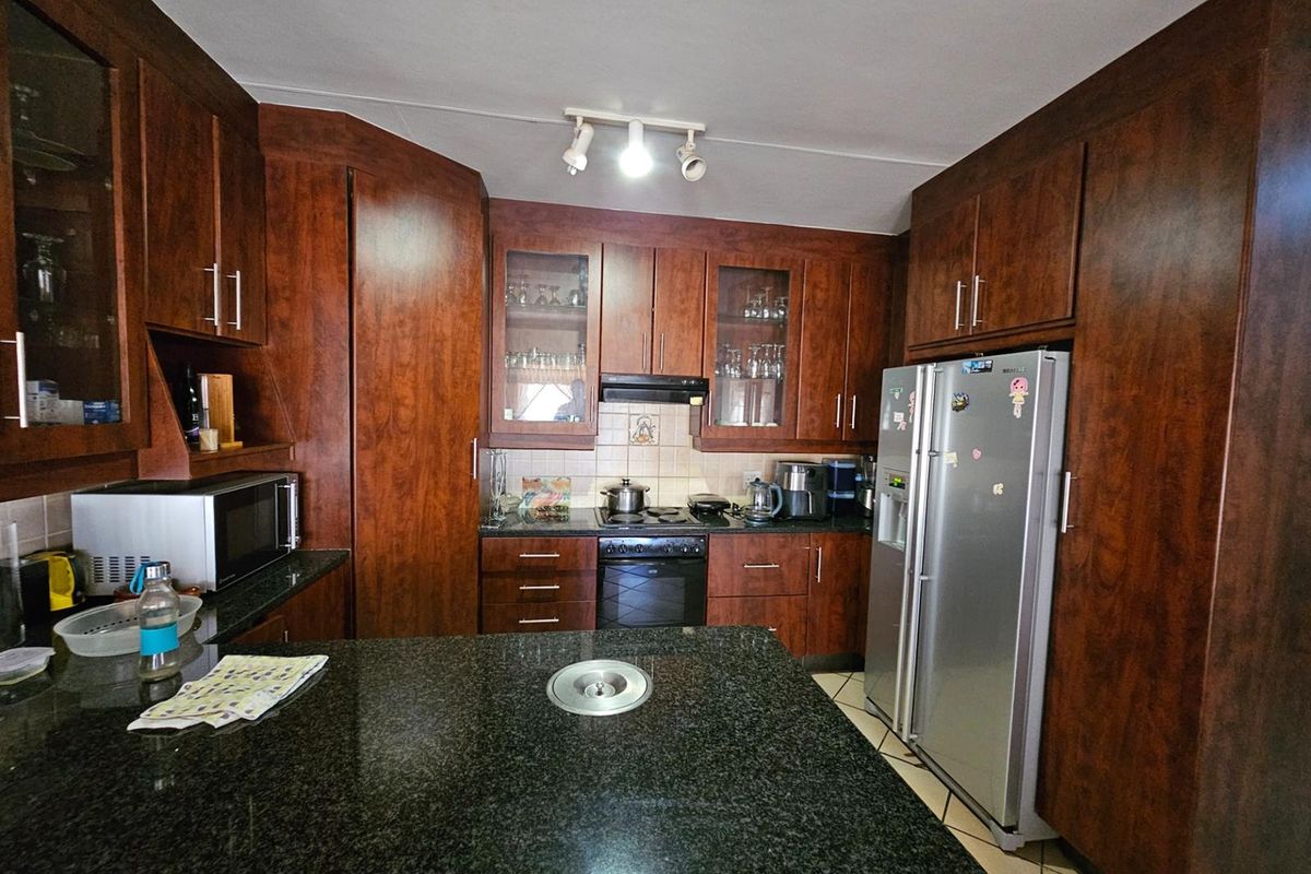 A functional kitchen featuring dark wood cabinetry, granite countertops, a built-in oven, hob, and extractor fan with a central island.
