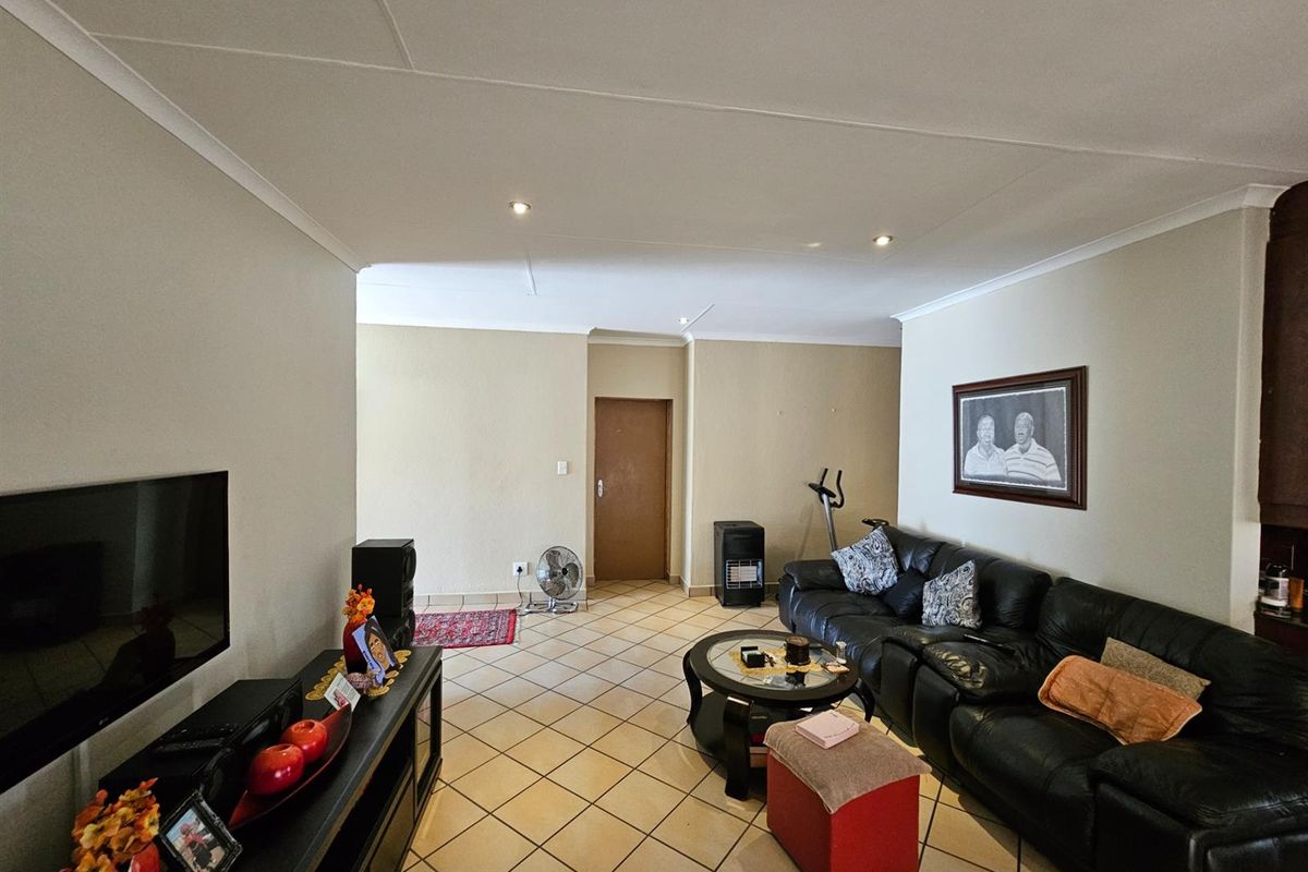A spacious living room featuring tiled flooring, recessed downlighting, and neutral wall finishes, providing a comfortable and functional area for relaxation.