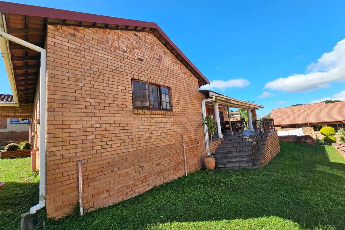 Exterior view of the rear brick facade featuring a raised patio area with stairs, overlooking a well-maintained lawn and garden space.