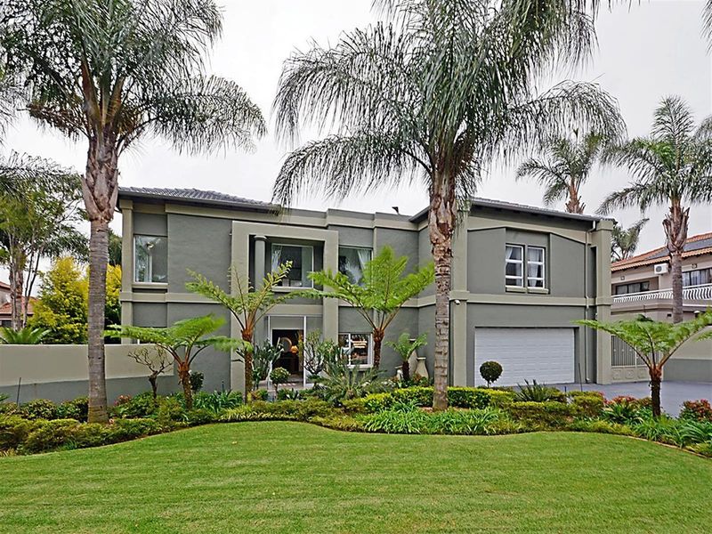 A well-maintained double-story residential property featuring a modern grey facade, integrated double garage, and established front garden with mature palm trees.