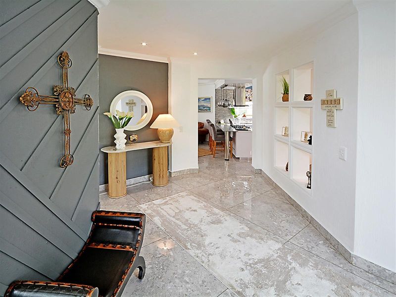 A bright and welcoming entrance hall featuring polished tile flooring, recessed ceiling lighting, and built-in display shelving, leading through to the open-plan kitchen area.