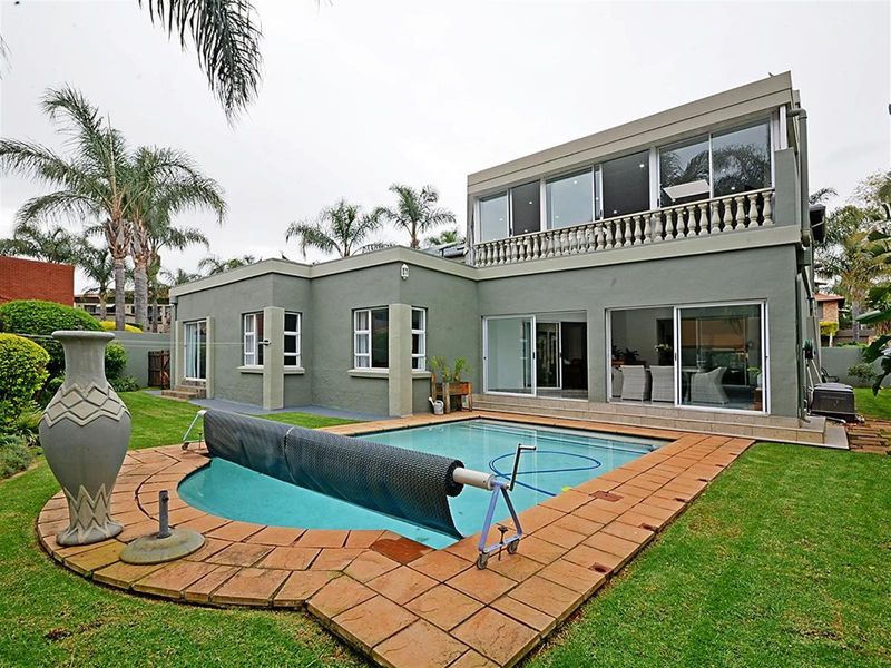 Rear view of the property featuring a swimming pool with a cover, paved surround, and a two-story building with sliding glass doors and balcony.