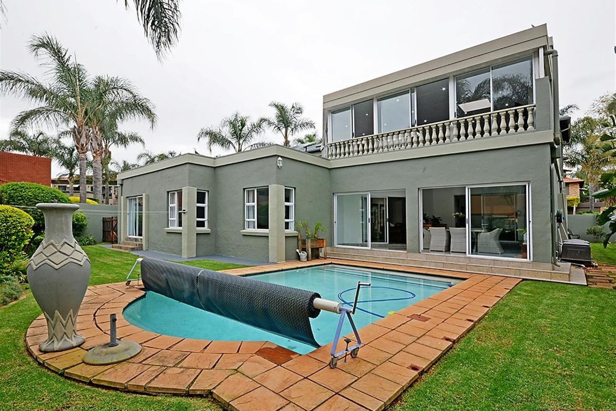Rear view of the property featuring a swimming pool with a cover, paved surround, and a two-story building with sliding glass doors and balcony.