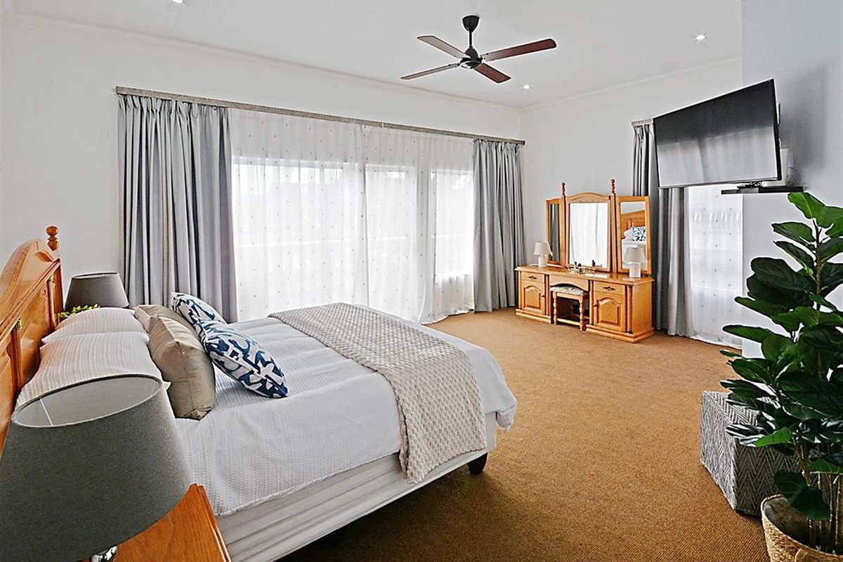 Spacious bedroom featuring neutral carpeting, recessed ceiling lighting, a modern ceiling fan, and large floor-to-ceiling curtains providing ample natural light.