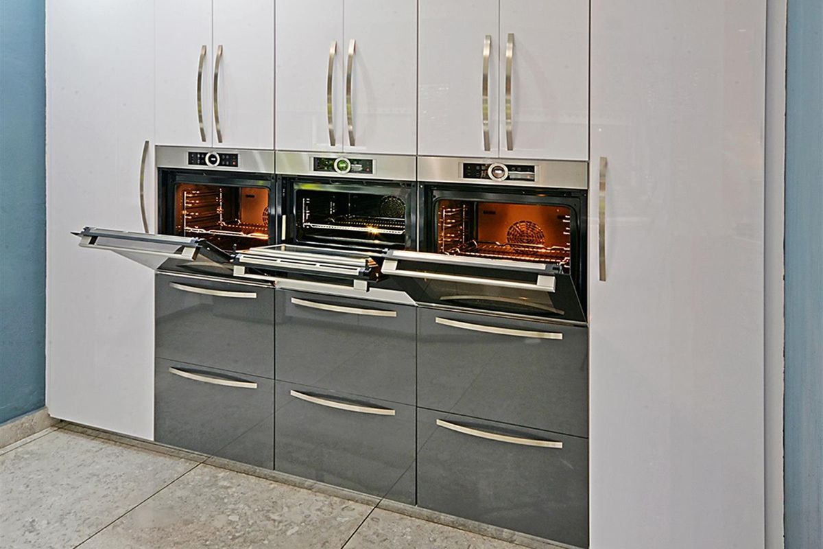 Modern kitchen featuring a bank of high-gloss cabinetry with three integrated built-in ovens and sleek stainless steel handles.
