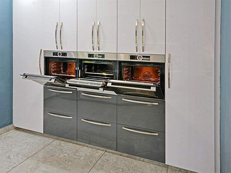 Modern kitchen featuring a bank of high-gloss cabinetry with three integrated built-in ovens and sleek stainless steel handles.