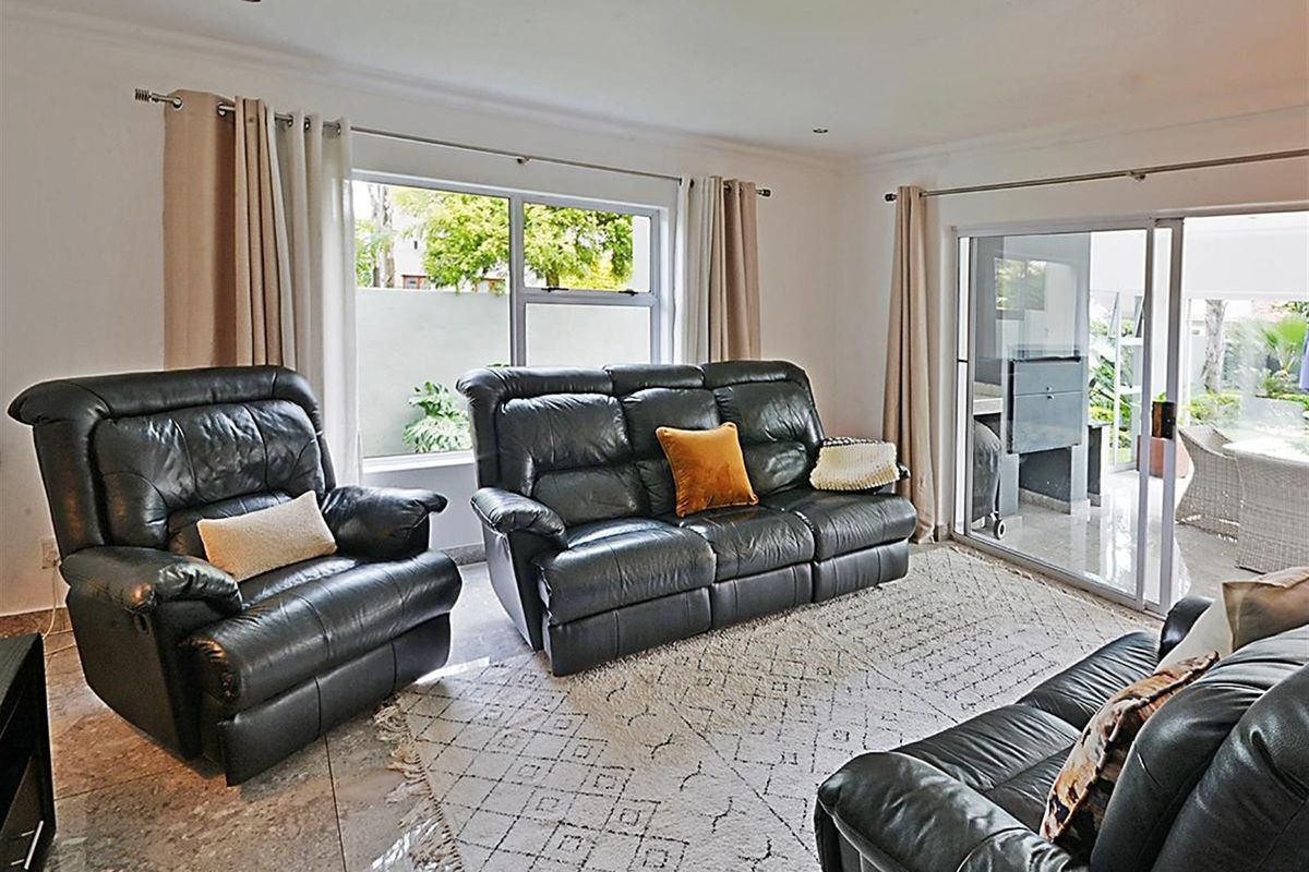 A bright living room featuring tiled flooring, recessed ceiling lighting, and large sliding glass doors providing direct access to an outdoor patio area.