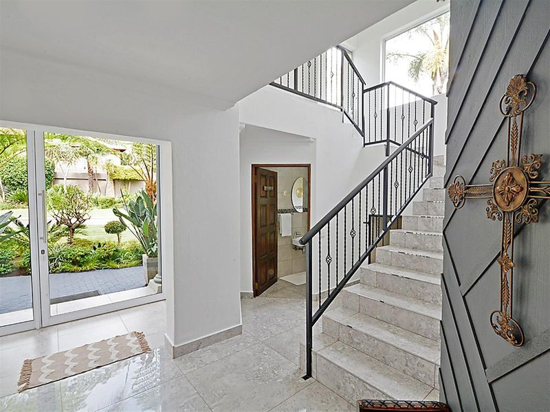Bright entrance hall featuring marble flooring, a staircase with wrought iron railings, and direct access to the garden through sliding glass doors.