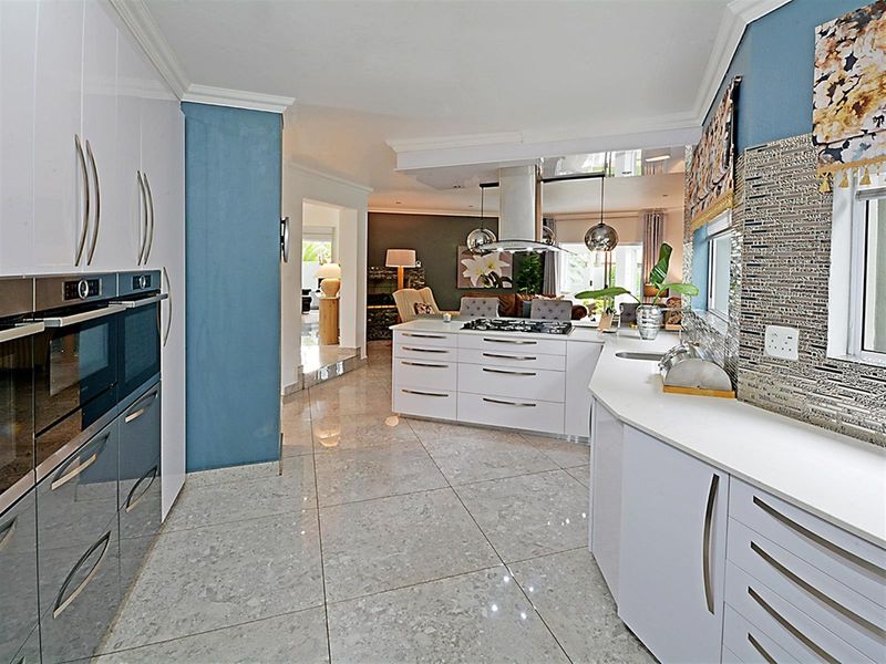 Modern open-plan kitchen featuring high-gloss cabinetry, a central island with a built-in gas hob, extractor fan, and sleek stone countertops.