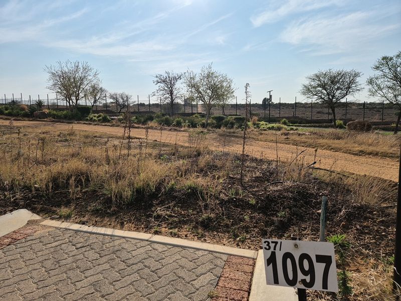 A vacant residential plot featuring a paved driveway entrance and perimeter fencing, offering a clear view of the undeveloped land.