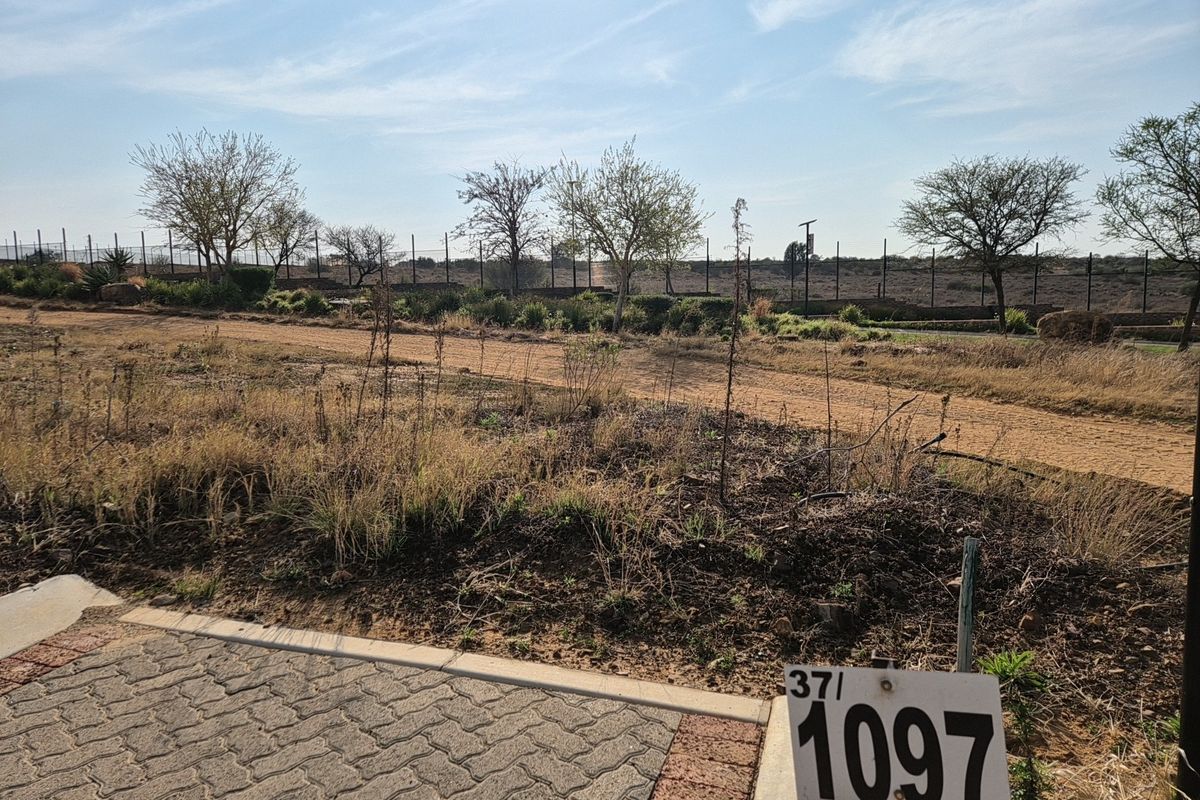 A vacant residential plot featuring a paved driveway entrance and perimeter fencing, offering a clear view of the undeveloped land.