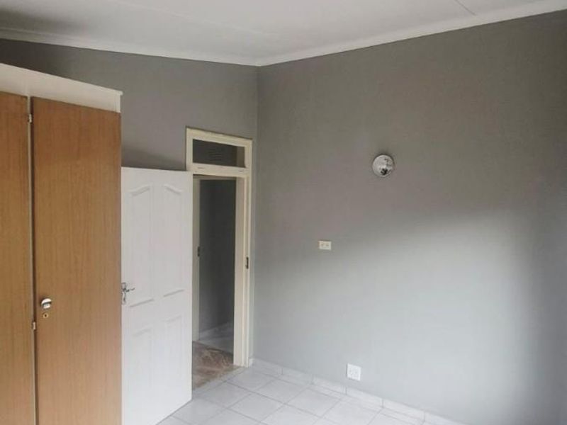 A clean, empty bedroom featuring neutral grey walls, tiled flooring, and a built-in wooden wardrobe.
