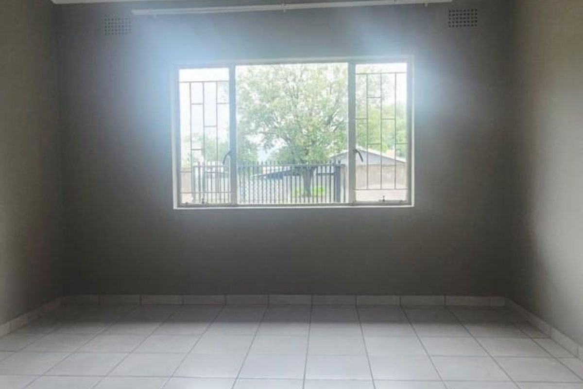 A bright, empty bedroom featuring neutral tiled flooring, security bars on the window, and simple cornice detailing.
