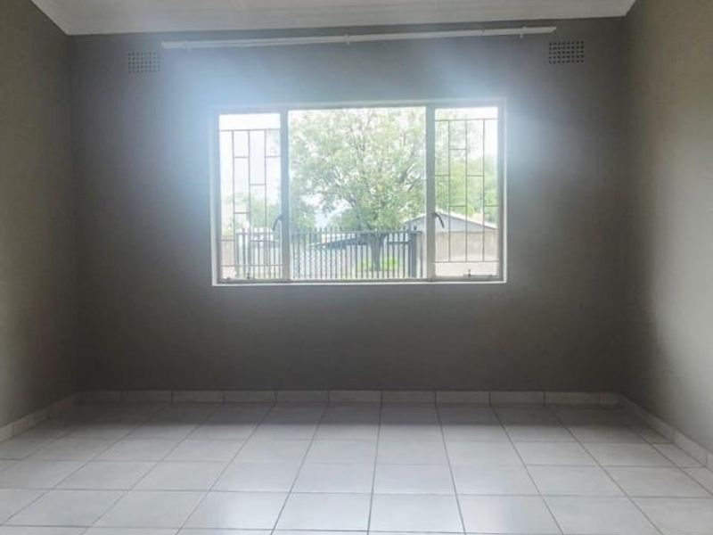 A bright, empty bedroom featuring neutral tiled flooring, security bars on the window, and simple cornice detailing.