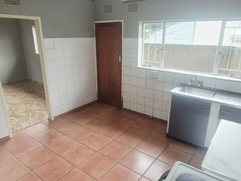 A functional kitchen featuring tiled flooring, a stainless steel sink, and a built-in electric stove, offering a blank canvas for modern renovation.