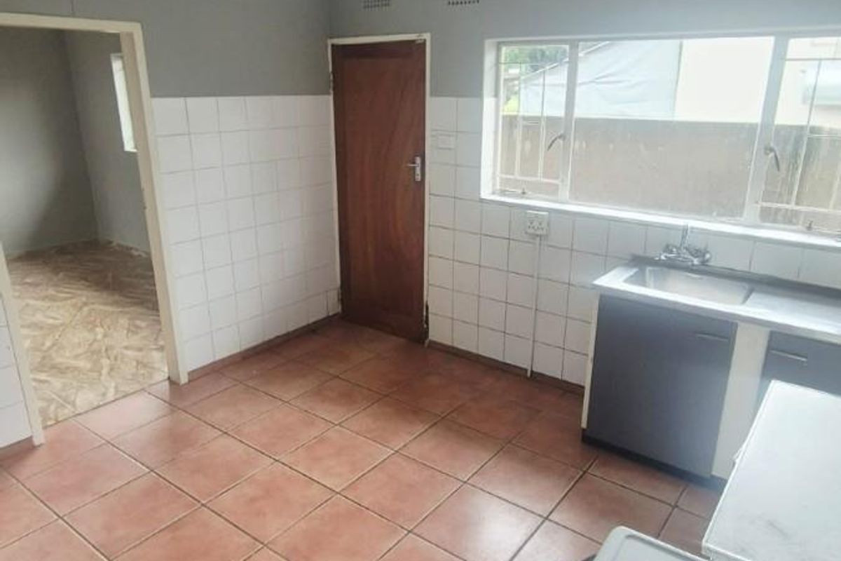 A functional kitchen featuring tiled flooring, a stainless steel sink, and a built-in electric stove, offering a blank canvas for modern renovation.