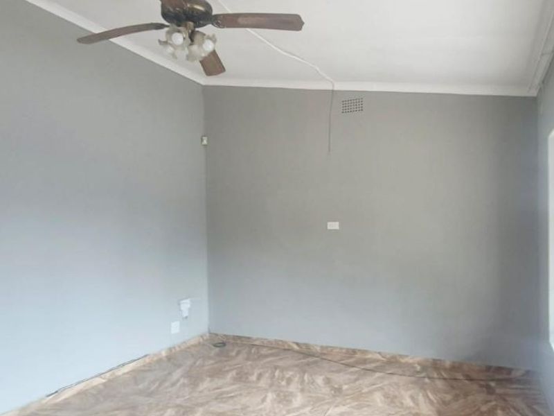 An empty living room featuring neutral grey walls, ceramic floor tiles, and a ceiling fan with exposed wiring.