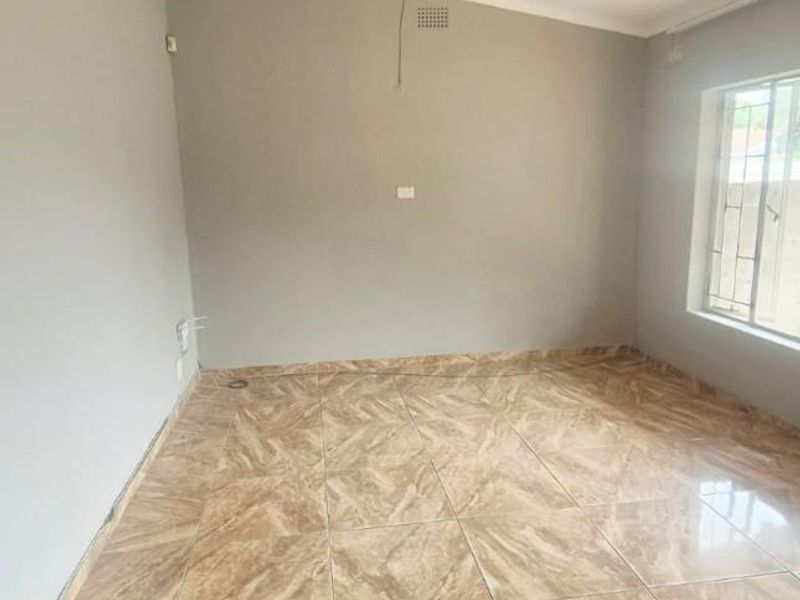 An empty living room featuring tiled flooring, a ceiling fan, and security bars on the window, with neutral wall finishes.