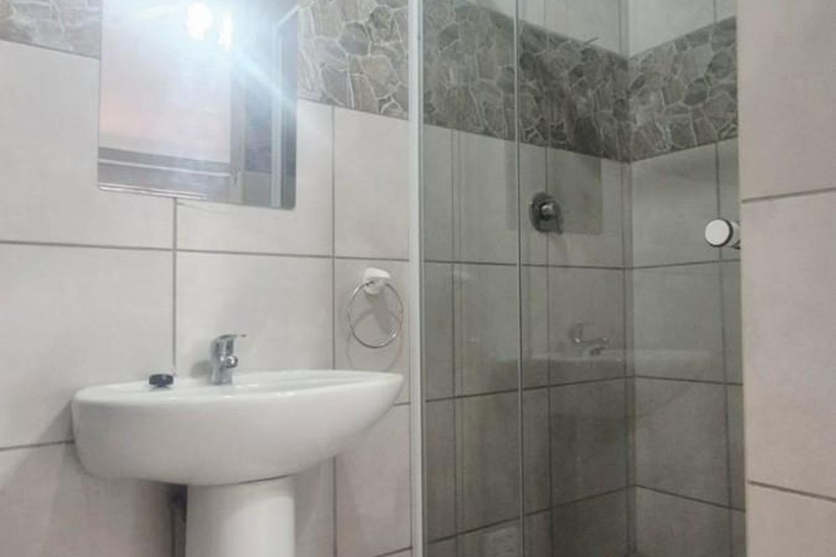 A clean, modern bathroom featuring a pedestal basin, a glass-enclosed shower, and neutral tiled finishes throughout.