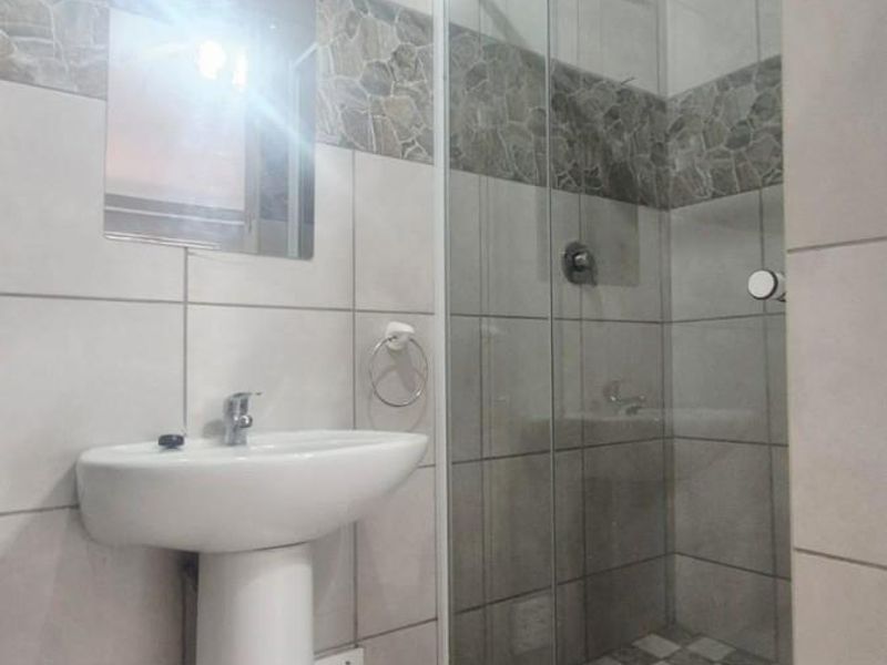 A clean, modern bathroom featuring a pedestal basin, a glass-enclosed shower, and neutral tiled finishes throughout.