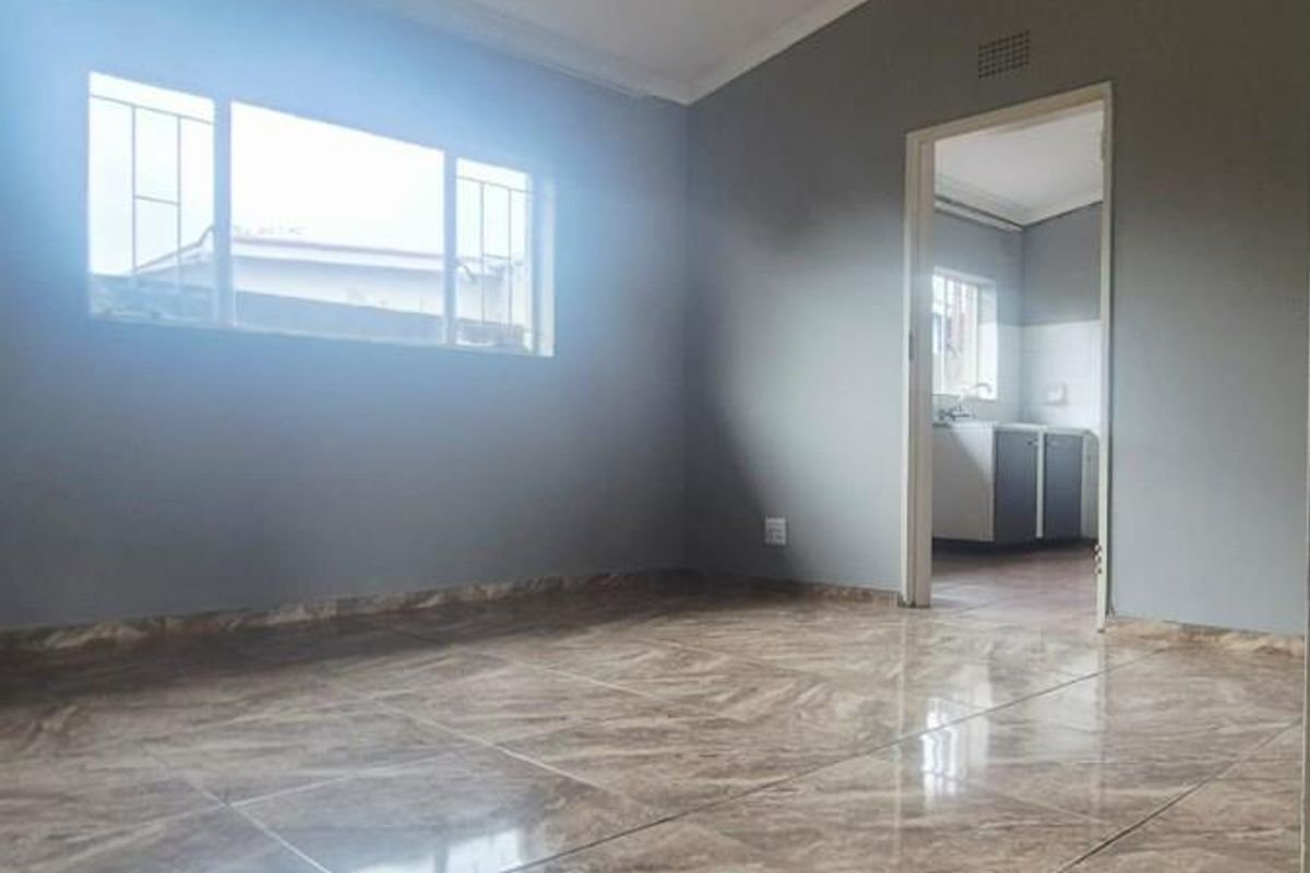 A bright, empty living area featuring polished marble-look floor tiles, neutral grey walls, and a doorway leading to an adjacent kitchen space.
