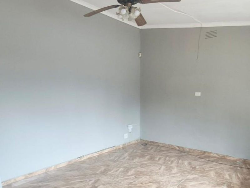 An empty living room featuring neutral grey walls, tiled flooring, and a ceiling fan, providing a blank canvas for personalization.