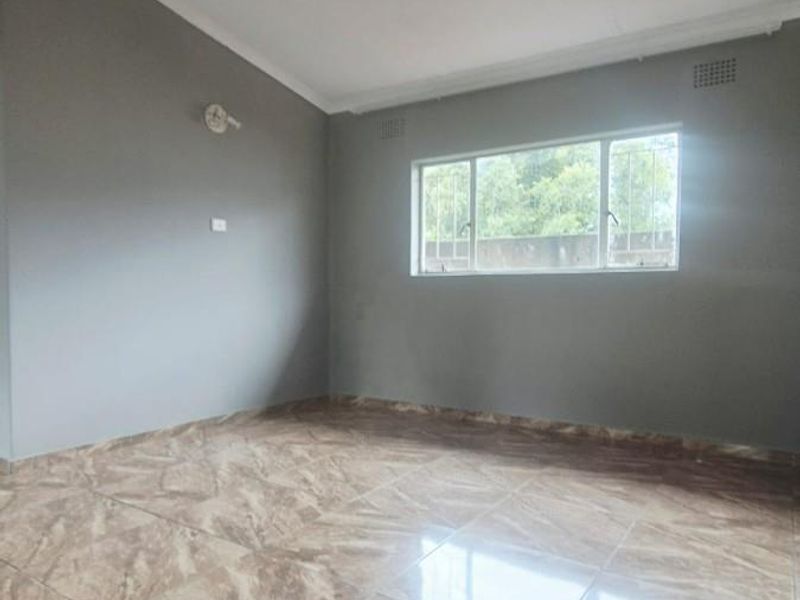 A bright, empty living room featuring neutral grey walls, polished marble-look floor tiles, and a window fitted with security bars.